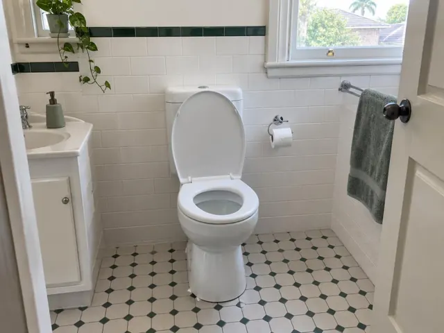Clean toilet in a tiled bathroom with white vanity, towel rail, and patterned floor in Maroubra