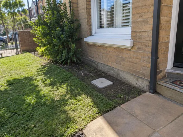 Flush white inspection cap on soil beside a brick house and lawn in Randwick